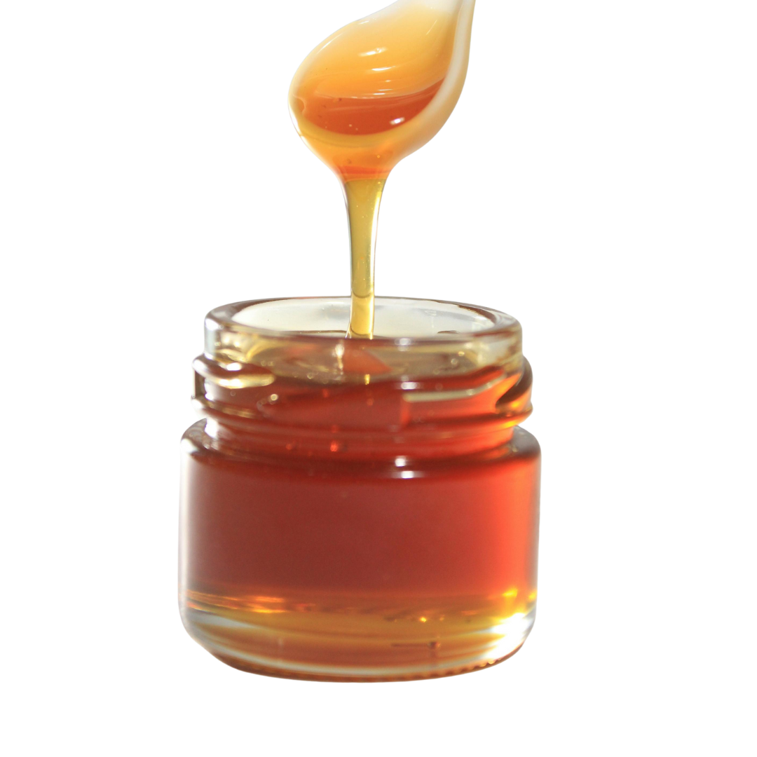 Honey being drizzled into a small glass jar on a white background